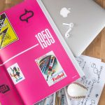 A creative workspace featuring a colorful open book, laptop, and drawing materials, ideal for design inspiration.