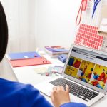 A woman in a blue jacket focused on a laptop screen in a colorful office workspace.